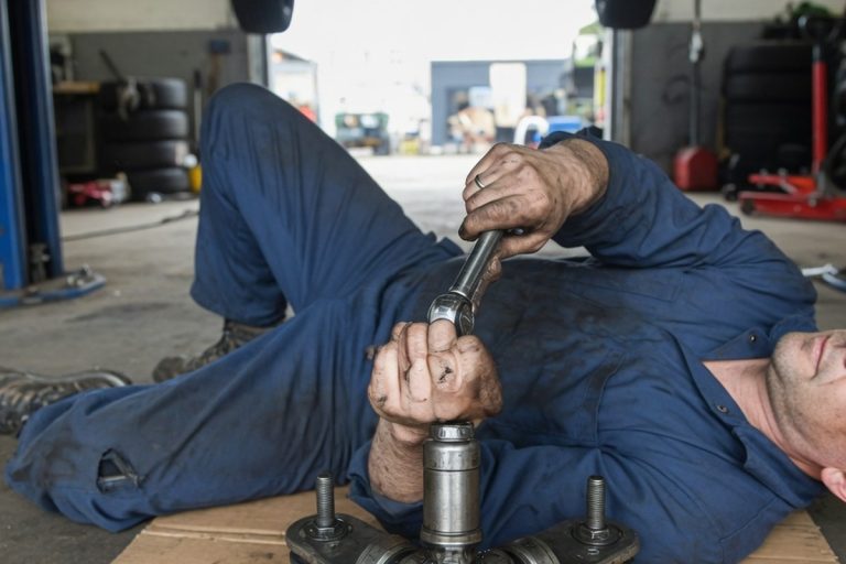Mécanicien inspectant le joint de cardan d'une voiture surélevée