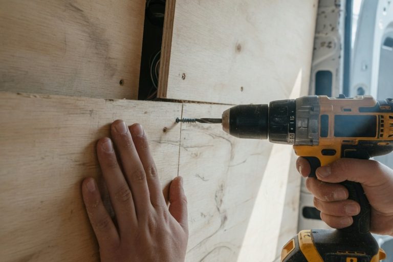 Mains fixant des panneaux bois dans un utilitaire avec perceuse